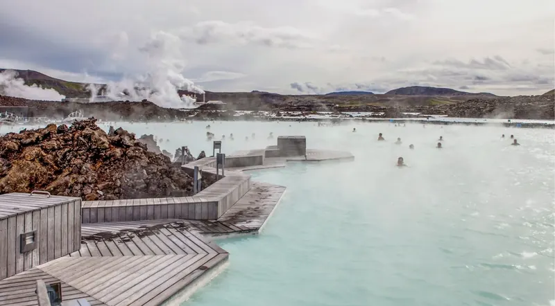 Bathers relaxing in the milky-blue geothermal water of the Blue Lagoon amid black lava rock and rising steam