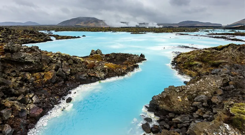 Vivid turquoise geothermal water winding between mossy black lava boulders