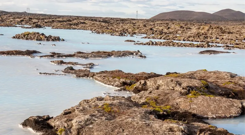 Milky-blue lagoon water threading through a vast lava field toward distant volcanic hills