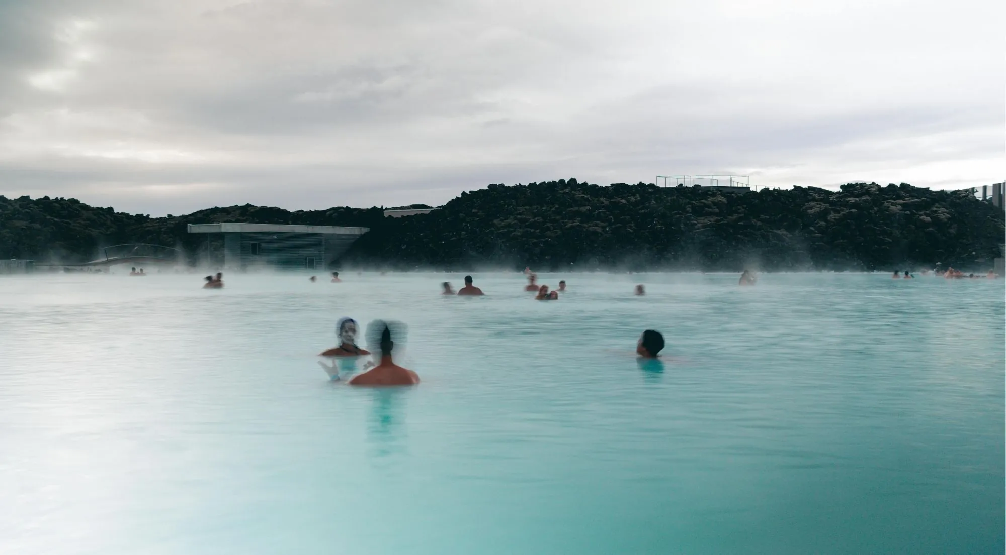 Guests wearing white silica mud masks while bathing in the warm turquoise lagoon water